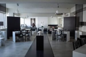 Sanctuary Mapo cafe interior in a minimalist black-and-white palette with concrete ceilings, white tables, cross-back chairs, globe lights, and curated shelves.