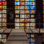 Colorful stained-glass wall inside a church-like interior on Yeongjong-do, with vibrant geometric panels, glossy black surfaces, and the MADE林 forest-inspired design.